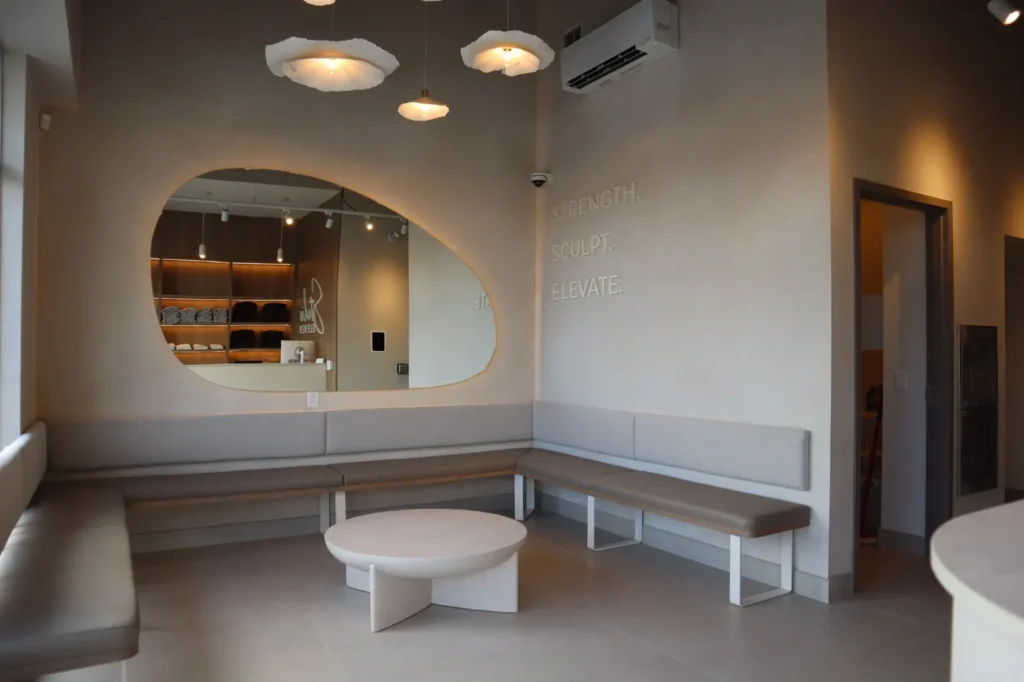 Reception lounge of a boutique pilates studio with two-tone sandy limewash walls and organic mirror