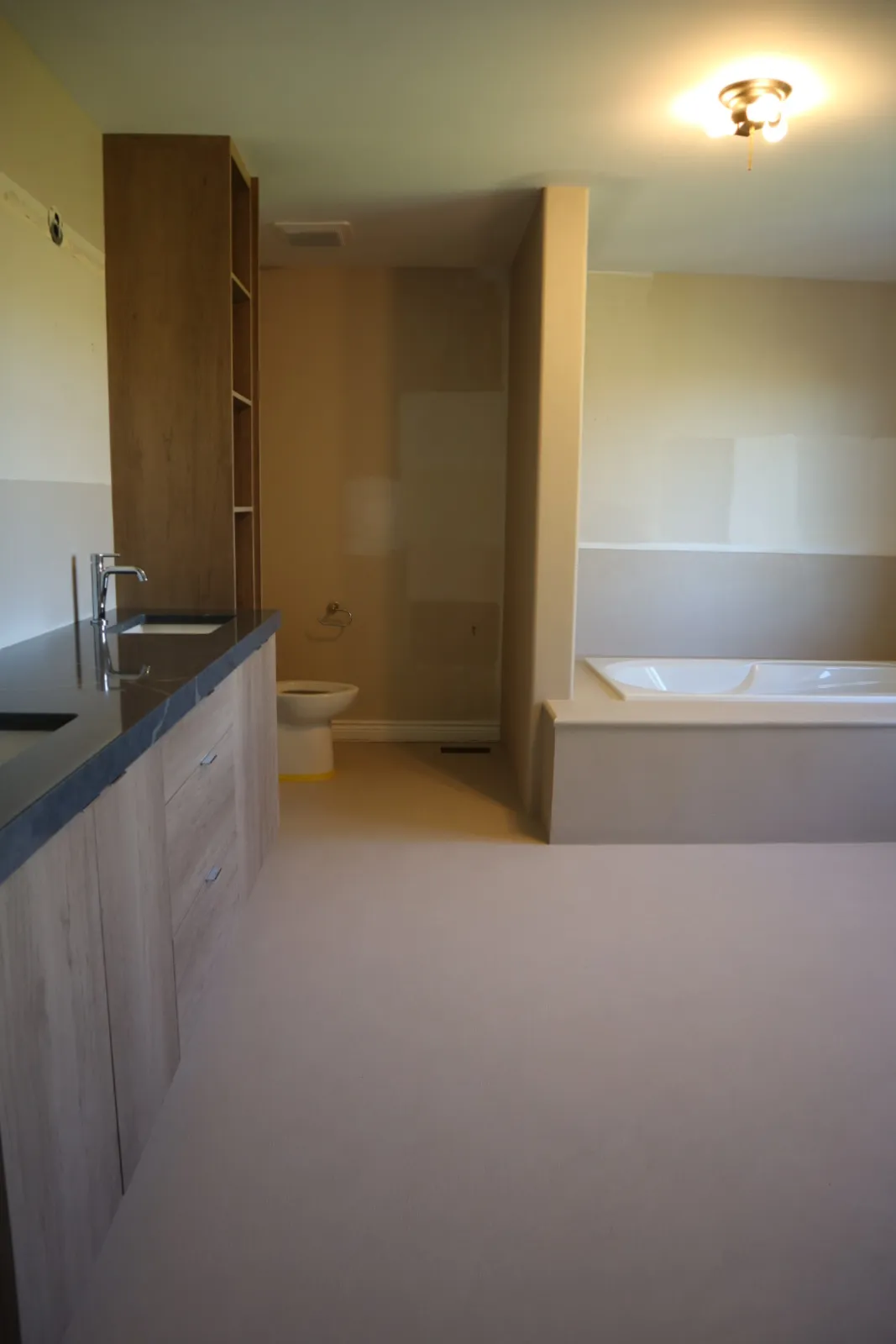 Grout-free microcement bathroom floor under a light wood vanity with dark stone counter